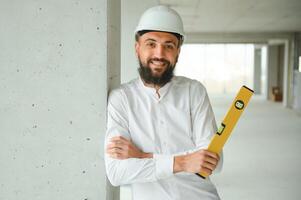 grave occupato giovane attraente Arabo industriale ingegnere nel difficile cappello con progetto disegni nel fabbrica interno. professionale e industria, costruttore architetto lavoro, lavoratore controllo opera a pianta interno foto