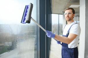 maschio professionale pulizia servizio lavoratore nel tuta da lavoro pulisce il finestre e negozio finestre di un' memorizzare con speciale attrezzatura. foto