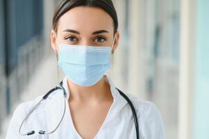 ritratto di giovane bellissimo femmina medico lavoratore, indossando uniforme e protettivo viso maschera foto