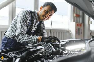 indiano auto meccanico in piedi e Lavorando nel servizio stazione. auto specialisti l'esame il sollevato macchina. professionale riparatori indossare meccanico uniforme nel blu colore. foto