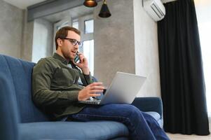 uomini Lavorando su il computer portatile computer nel il suo camera. casa opera o studia, libero professionista concetto. giovane uomo seduta rilassato su divano con il computer portatile. moderno uomo d'affari utilizzando il computer portatile. foto