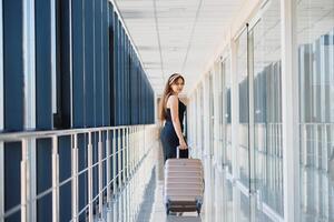 elegante donna nel un' nero vestito con un' valigia nel il aeroporto terminale in attesa per un' aereo. foto