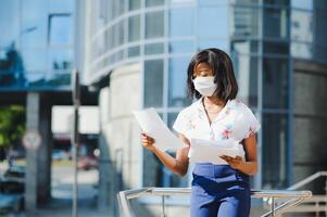 vicino su giovane afro americano donna d'affari indossare proteggere maschera, fissando a il telecamera. foto