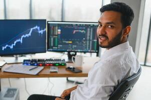 ritratto di un' positivo riuscito indiano o arabo commerciante, azione mercato broker, crypto grafici su il computer portatile schermo foto