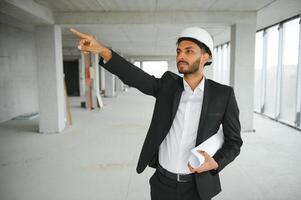 indiano costruzione luogo manager in piedi indossare casco, pensiero a costruzione luogo. ritratto di misto gara Manuale lavoratore o architetto. foto