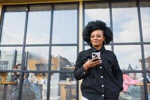 allegro africano donna utilizzando inteligente Telefono all'aperto foto