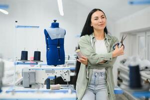 giovane sarta donna cuce Abiti su Lavorando tavolo. sorridente sarta e sua mano vicino su nel officina. foto