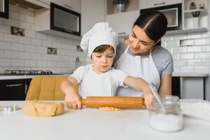 poco ragazzo porzione il suo madre con il cottura al forno nel il cucina in piedi a il contatore a fianco sua impasto il Impasto per il torta foto