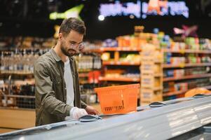 ritratto di sorridente bello uomo drogheria shopping nel supermercato, la scelta cibo prodotti a partire dal mensola foto