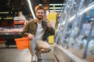 bello giovane uomo dai un'occhiata il frigoriferi per congelato cibo nel il supermercato. foto