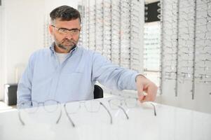 bello anziano uomo la scelta occhiali telaio nel ottico negozio. foto