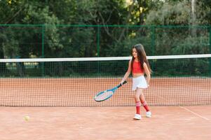 bambino giocando tennis su all'aperto Tribunale. poco ragazza con tennis racchetta e palla nel sport club. attivo esercizio per bambini. estate attività per bambini. formazione per giovane ragazzo. bambino apprendimento per giocare foto