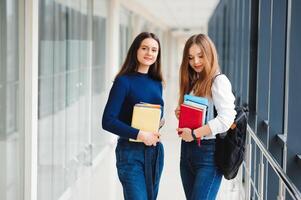 Due femmina studenti In piedi nel il corridoio di il Università con libri foto