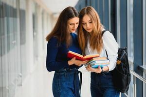 Due giovane femmina studenti in piedi con libri e borse nel il corridoio Università A proposito di ogni Altro. foto