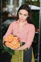 carino ragazza fioraio raccoglie un' mazzo di Rose nel un' fiore negozio. un' bellissimo fioraio crea un' composizione di fiori. ragazza tagli fiori e rimuove stantio le foglie foto