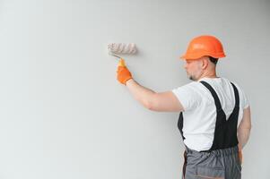 pittore uomo pittura il parete nel casa, con dipingere rullo e bianca colore dipingere. camera lavori di ristrutturazione a Casa. foto