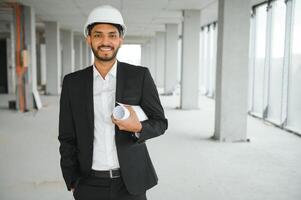 indiano costruzione luogo manager in piedi indossare casco, pensiero a costruzione luogo. ritratto di misto gara Manuale lavoratore o architetto. foto