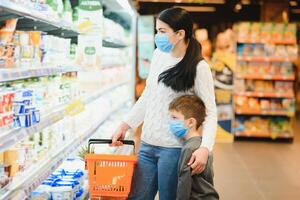 autentico tiro di madre e figlio indossare medico maschere per proteggere loro stessi a partire dal malattia fabbricazione shopping per drogheria insieme nel supermercato foto