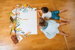 bambini disegno su pavimento su carta. prescolastico ragazzo e ragazza giocare su pavimento con educativo giocattoli - blocchi, treno, Ferrovia, aereo. giocattoli per prescolastico e asilo. bambini a casa o asilo nido. superiore Visualizza. foto