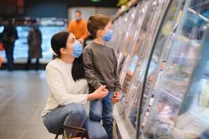 autentico tiro di madre e figlio indossare medico maschere per proteggere loro stessi a partire dal malattia fabbricazione shopping per drogheria insieme nel supermercato foto