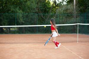 bambino giocando tennis su all'aperto Tribunale. poco ragazza con tennis racchetta e palla nel sport club. attivo esercizio per bambini. estate attività per bambini. formazione per giovane ragazzo. bambino apprendimento per giocare foto