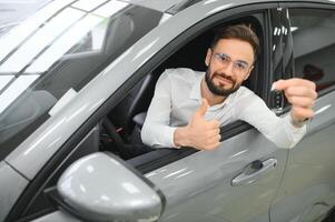 sì, quello è mio nuovo macchina. cliente nel auto concessionaria. giovane uomo con chiavi nel mano foto