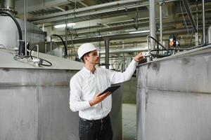 vicino su di giovane caucasico sorridente lavoratore con casco su testa utilizzando tavoletta per opera mentre in piedi nel magazzino. foto