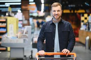 giovane uomo acquisto drogheria a il supermercato. altro i clienti nel sfondo. consumismo concetto. foto