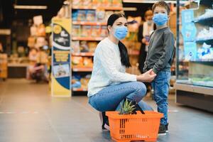 autentico tiro di madre e figlio indossare medico maschere per proteggere loro stessi a partire dal malattia fabbricazione shopping per drogheria insieme nel supermercato foto