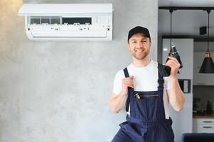 sorridente giovane maschio elettricista riparazione condizionatore nel cliente casa. uomo meccanico o riparatore fix filtri nel aria condizione dispositivo a cliente Casa foto