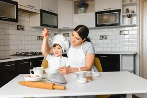 un' giovane e bellissimo mamma è preparazione cibo a casa nel il cucina, lungo con sua poco figlio foto