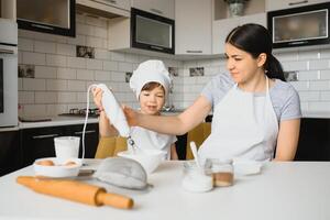 un' giovane e bellissimo mamma è preparazione cibo a casa nel il cucina, lungo con sua poco figlio foto