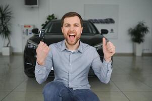 visitare auto concessionaria. bello barbuto uomo è accarezzando il suo nuovo auto e sorridente. foto