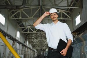 un' giovane bello dipendente di un' moderno fabbrica nel un' bianca difficile. nel il sfondo è un' grande negozio per il produzione. foto