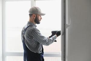 operaio nel tuta da lavoro installazione o regolazione plastica finestre nel il vivente camera a casa foto