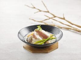 giapponese qualcuno con cernia filetto nel pesce la minestra servito nel un' piatto lato Visualizza su grigio sfondo foto