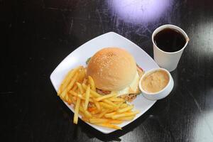 pollo formaggio hamburger con patatine fritte, mayo tuffo e bibita bevanda servito nel un' piatto isolato su buio sfondo lato Visualizza di indiano speziato Fast food foto