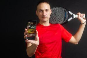 uomo Tenere paddle racchetta e smartphone con gli sport scommesse su nero sfondo foto