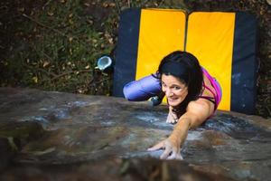 una bellissima ragazza che pratica il boulder con il crash pad che la protegge foto