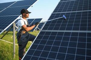 alternativa energia pianta lavoratore nel uniforme pulizia solare pannelli con Mocio. bello afroamericano assunzione cura di attrezzatura. foto