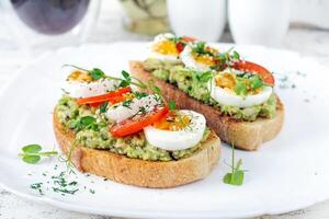 delizioso crostini con avocado, bollito uovo, pomodori e microgreen su un' bianca piatto. salutare mangiare, prima colazione. cheto dieta cibo. di moda cibo. foto