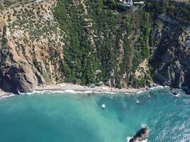 aereo Visualizza a partire dal sopra su calma azzurro mare e vulcanico roccioso sponde. piccolo onde su acqua superficie nel movimento sfocatura. natura estate oceano mare spiaggia sfondo. nessuno. vacanza, vacanza e viaggio concetto foto