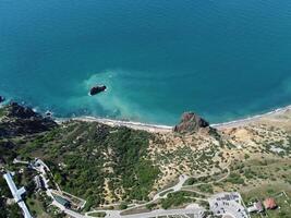 aereo Visualizza a partire dal sopra su calma azzurro mare e vulcanico roccioso sponde. piccolo onde su acqua superficie nel movimento sfocatura. natura estate oceano mare spiaggia sfondo. nessuno. vacanza, vacanza e viaggio concetto foto