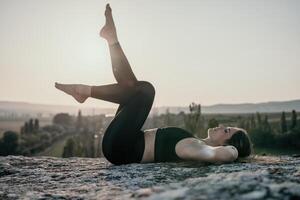 fitness donna. bene guardare mezzo anziano donna con lungo capelli, fitness istruttore nel ghette e cime fare allungamento e pilates su il roccia vicino foresta. femmina fitness yoga routine concetto. foto