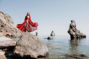 donna viaggio mare. giovane contento donna nel un' lungo rosso vestito in posa su un' spiaggia vicino il mare su sfondo di vulcanico rocce, piace nel Islanda, condivisione viaggio avventura viaggio foto