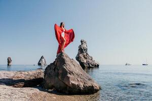 donna viaggio mare. giovane contento donna nel un' lungo rosso vestito in posa su un' spiaggia vicino il mare su sfondo di vulcanico rocce, piace nel Islanda, condivisione viaggio avventura viaggio foto