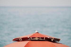 rosso spiaggia ombrello su il sfondo di il blu mare oceano. spiaggia paesaggio. estate viaggio e vacanze concetto. foto