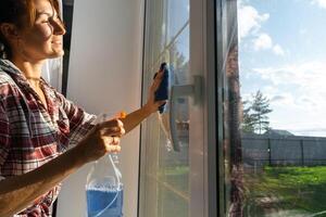 donna manualmente lavaggi il finestra di il Casa con un' straccio con spray addetto alle pulizie e Mocio dentro il interno con bianca tende. ripristino ordine e pulizia nel il molla, pulizia servise foto