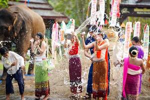 gruppo di tailandese donne e bambini merce tailandese tradizionale vestito giocare per spruzzi acqua su il tailandese nuovo anni giorno o Songkran Festival nel un' divertimento modo su elefante e mucchio di sabbia sfondo. foto