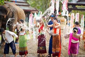 gruppo di tailandese donne e bambini merce tailandese tradizionale vestito giocare per spruzzi acqua su il tailandese nuovo anni giorno o Songkran Festival nel un' divertimento modo su elefante e mucchio di sabbia sfondo. foto